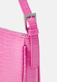 Różowa torba ze skóry krokodyla z wytłoczeniem, wyposażona w srebrny zamek błyskawiczny, regulowany pasek i dokładne przeszycia. Posiada boczną kieszeń na dodatkowe przechowywanie.