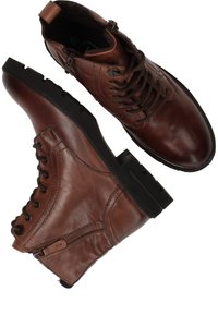 Bruine leren enkelschoenen met veters en een rits aan de zijkant, ronde neus, zwarte rubberen zool en stiksels langs de zijkanten.