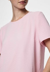 T-shirt rosa a maniche corte con scollo rotondo, caratterizzato da un tessuto testurizzato e una vestibilità rilassata. Il tessuto presenta sottili motivi a onde.