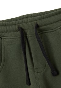Pantaloni della tuta verde oliva con una texture morbida, vita elastica e lacci neri; comprendono tasche laterali e dettagli cuciti.