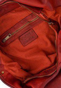 Binnenkant van een rode leren handtas, met een gladde textuur, een ritszak en een gelabelde leren tag. Voering van bijpassende rode stof.