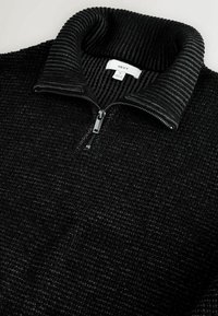 Juodas užtrauktukas megztinis su tekstūruotu paviršiumi ir raukiniais apykaklėje. Yra centrinis užtrauktukas ir etiketė matoma apykaklės viduje.