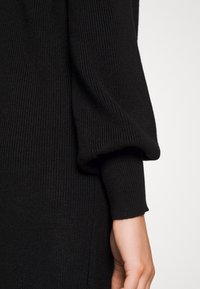 Czarny prążkowany sweter z detalem bufiastych rękawów. Miękka tekstura i dopasowane mankiety podkreślają design ubrania.