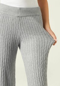 Pantalones de punto gris con cintura acanalada, patrones texturizados y bolsillos laterales, hechos de un material suave y elástico.