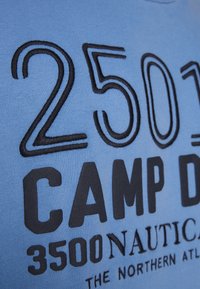 Blaues T-Shirt mit großen schwarzen, aufgestickten Zahlen "2501" und dem Wort "CAMP" sowie darunter in fetten Buchstaben zusätzlichem Text "3500 NAUTICAL".