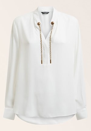Blouse blanche à manches longues avec col en V, cordons chaîne dorés attachés à deux boutons dorés décoratifs au col.