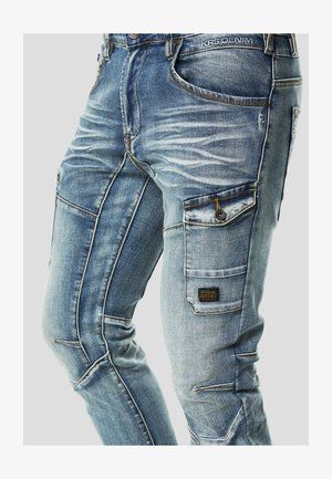 Lichtblauwe denim cargobroek met verouderde details, meerdere zakken, donkere stiksels en een geweven label op de zijzak.
