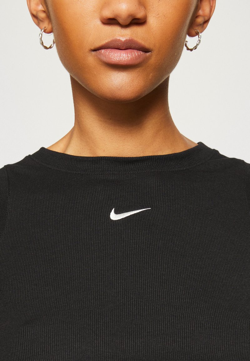 T-shirt noire à côtes avec un col rond et un logo Nike blanc sur la poitrine. Présente une texture douce et une coupe ajustée.