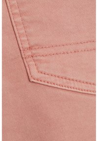 Gros plan sur un tissu rose montrant une couture détaillée dans un angle de poche rectangulaire, mettant en valeur la texture et les lignes de couture.