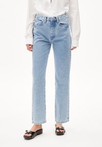 Jeans de tiro alto azules claros con diseño de pierna recta, cinco bolsillos, un ligero desgastado y cierre de botón. Usados con sandalias de plataforma negras.