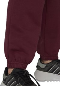Vinröda sweatpants med elastiska mudd, kombinerade med svarta och grå sneakers med en tjock vit sula och randig design på sidan.