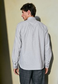 Grey plaid button-up shirt with long sleeves and single-button cuffs, made from a soft fabric, featuring a classic collar and curved hem.