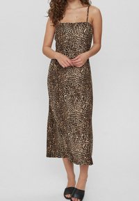 Vestido maxi de estampado de leopardo con un corsé ajustado, tirantes finos y una falda fluida. La tela es suave con un ligero brillo. Sandalias negras.
