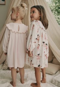 Kaksi lasta wear polvenmittaisia yöhousuja. Toinen on yksivärinen vaaleanpunainen, jossa on frillikaulus ja nappi; toinen puolestaan esittää balettitanssijan kuviota.