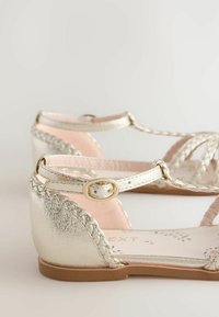Metallic silver sandals with braided straps and a side buckle, featuring a soft pink insole and flat brown sole.