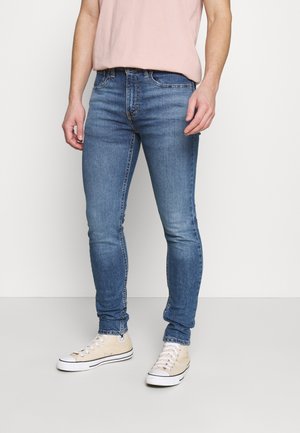 Jeans skinny bleu clair en denim avec une texture lisse. Dotés d'un design classique à cinq poches et d'un léger dégradé. Portés avec des baskets beiges.