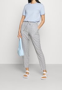 Světle modré tričko, šedé kalhoty s vysokým pasem a vzorem, s šňůrkou, bílé ploché sandály a malá světle modrá kabelka přes rameno.