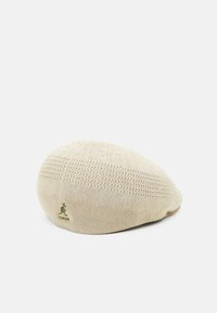 Kangol-baret i beige stickat material, med en texturerad yta med växlande mönster. Grön logotyp syns på sidan.