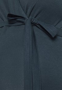 Abito verde scuro caratterizzato da una texture morbida, un dettaglio con fiocco in vita e un sottile design a righe. Il tessuto sembra leggero e aderente.