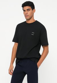 T-shirt de algodão preto com gola redonda e mangas curtas. Apresenta dois pequenos logótipos brancos "SAMSØE" no peito. Textura suave, corte descontraído.