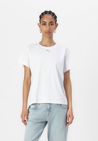 Tricou alb din bumbac, cu mâneci scurte, având un decolteu rotund și un mic logo pe piept. Asortat cu blugi din denim albastru deschis.