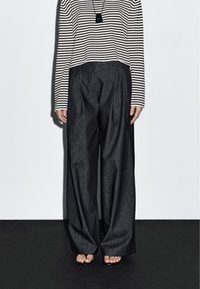 Zwarte wijde spijkerbroek met plooien, gecombineerd met een cropped zwart-wit gestreept langemouwen top en simpele sandalen.
