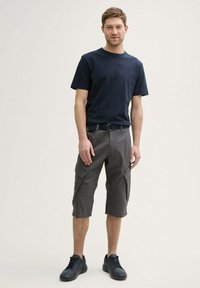 Navyblaues Baumwoll-T-Shirt, kombiniert mit grauen Cargoshorts, die Taschen, Gürtelschlaufen und eine lockere Passform besitzen. Getragen mit dunklen Sneakers.