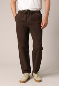 Bruine katoenen broek met een elastische tailleband en trekkoord, voorzien van zijzakken en een relaxte pasvorm, gecombineerd met off-white schoenen.