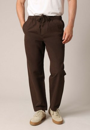 Bruine katoenen broek met een elastische tailleband en trekkoord, voorzien van zijzakken en een relaxte pasvorm, gecombineerd met off-white schoenen.