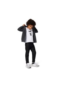 Šedá mikina na zip přes bílé tričko s grafickým motivem, doplněná tmavými džíny a bílými teniskami s černými detaily.