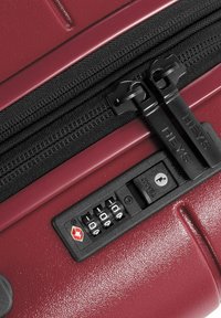 Close-up of red suitcase zipper with black dual pull tabs and built-in TSA combination lock showing dials set to 0-0-0.