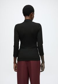 Čierny top s dlhým rukávom s priliehavým strihom a detailom v podobe zadného švu, doplnený širokými bordovými nohavicami z hladkej látky.