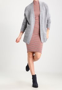 Gray knit cardigan over a pink striped dress, featuring a bodycon shape and long sleeves. Black ankle boots complete the look.