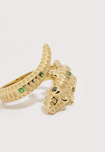 Złoty pierścionek z teksturowanym wzorem przypominającym krokodyla, ozdobiony zielonymi i czarnymi kamieniami szlachetnymi, gładką powierzchnią i błyszczącym wykończeniem.