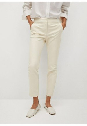 Slim-Fit cremefarbene Hose mit Seitentaschen, getragen mit passenden cremefarbenen flachen Schuhen und einem weißen Hemd mit Knöpfen und hochgekrempelten Ärmeln.