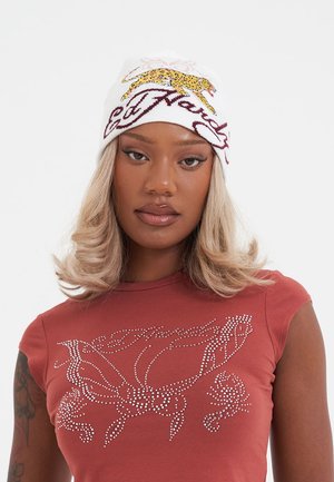 White knit beanie featuring a yellow leopard design and burgundy text. Soft texture with a fitted shape, worn above the forehead.