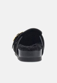 Chausson en daim noir avec une doublure en fourrure noire rembourrée, une semelle noire élégante, et un accent de boucle dorée sur le côté.