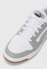 Grå og hvid sneaker med perforeret tåboks, flade snørebånd og Puma-logo på tungen. Har en tekstureret gummisål og en glat læderoverdel.