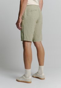 Lichtgroene shorts van gestructureerde stof met een trekkoord in de taille en twee achterzakken, gedragen met crèmekleurige sneakers en gestreepte sokken.
