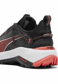 Scarpa da ginnastica nera e rossa con tomaia in rete, suola intermedia bianca spessa, suola testurizzata e dettagli riflettenti. Presenta il marchio PUMAGRIP e NITRO.