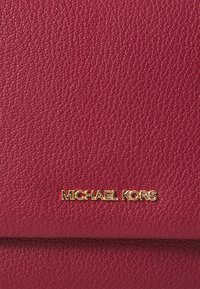Rote, strukturierte Lederbörse mit goldfarbenem "MICHAEL KORS"-Logo. Das Design ist schlank, mit sichtbaren Nähten und einer glatten Oberfläche.