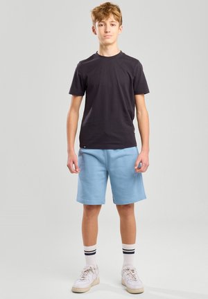 Camiseta de algodón negra, pantalones cortos de sudadera azul claro, zapatillas blancas con detalles en crema y calcetines de rayas hasta el tobillo. Diseño simple y casual.