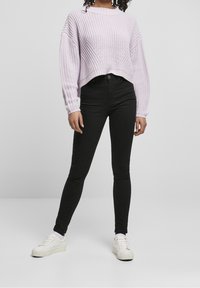 Maglione a maglia di un leggero viola con un design corto, abbinato a jeans skinny neri e sneakers bianche. Presenta una texture a coste e maniche oversize.