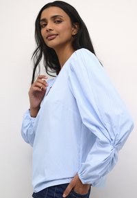 Blusa a maniche lunghe a strisce blu chiaro con maniche a sbuffo e polsini elasticizzati, caratterizzata da una scollatura a V e una vestibilità rilassata.
