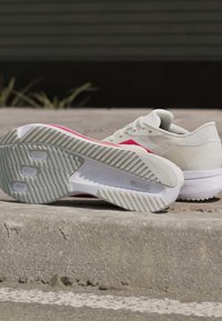 Par hvide løbesko med pink accenter hvilende på beton, den ene viser sålen med "ADIZERO" branding.
