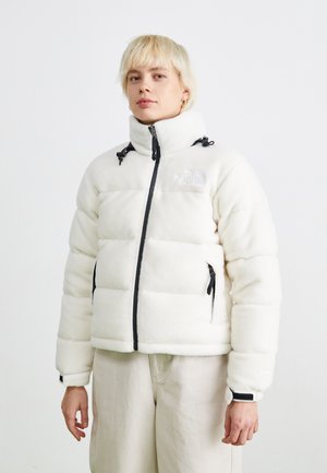 Witte pufferjack met een hoge kraag, ritssluiting en zwarte accenten. Heeft een logo op de borst en ritszakken aan de zijkant. Zachte textuur.