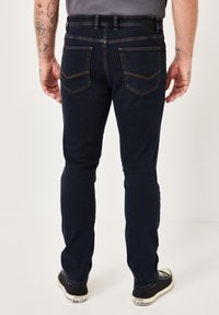 Dark blue denim jeans with a slim fit, five pockets, and contrasting stitching. Worn with black sneakers with white accents.