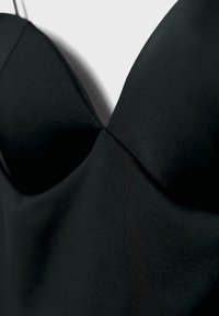 Vêtement noir sans manches avec bonnets moulés et détails en tissu lisse, montré en gros plan sur un fond uni.