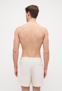 Bermudas blanches en tissu éponge avec une texture douce, ceinture élastique et une petite poche arrière. Le modèle est vu de dos.