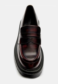 Dark burgundy leather loafer with thick black rubber sole and classic penny strap detail, photographed from above.